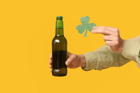 Hands of man with bottle of beer and shamrock on yellow background. St. Patrick's Dayの写真素材