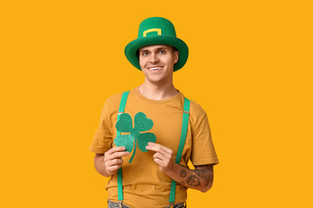 Happy young man in leprechaun's hat and with clover on yellow background. St. Patrick's Day