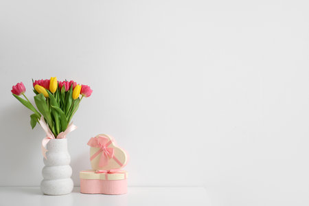Vase with tulips and gift boxes on shelf near light wall. International Women's Day celebrationの写真素材
