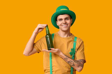 Happy young man in leprechaun's hat and with bottle of beer on yellow background. St. Patrick's Dayの写真素材