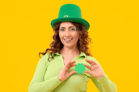 Woman in green hat and with paper clover on yellow background. St. Patrick's Day celebration