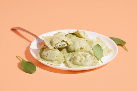 Plate of tasty ravioli with vegetables on orange background
