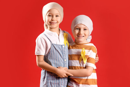 Cute little children after chemotherapy with yellow ribbons on red background. Childhood cancer awareness conceptの写真素材