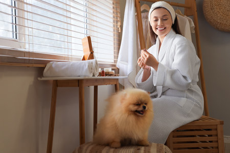 Young woman with cute Pomeranian dog applying lipstick in bathroomの写真素材