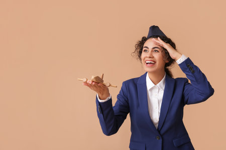 Beautiful African-American stewardess with toy plane on beige backgroundの写真素材