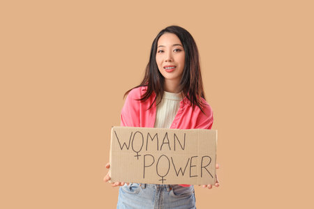Young Asian girl holding paper with text WOMAN POWER on beige backgroundの写真素材