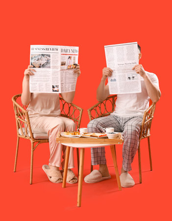 Young couple reading newspapers during breakfast on red background. Valentine's Day celebrationの写真素材