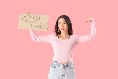 Young Asian girl holding paper with text WOMAN POWER on pink backgroundの写真素材