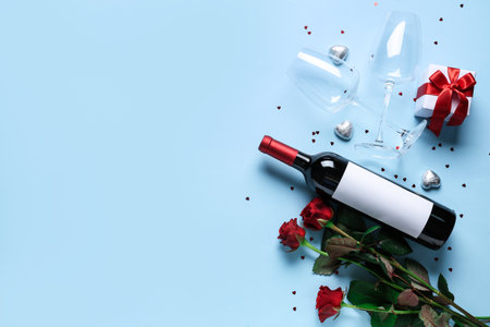 Bottle of wine with glasses, roses and gift on blue background. Valentine's Day celebrationの写真素材