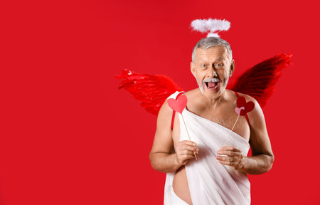 Mature man dressed as Cupid with hearts on red background. Valentine's Day celebrationの写真素材
