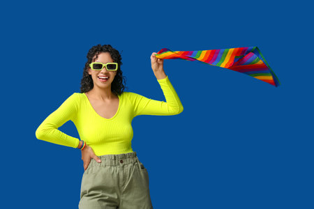 Happy African-American woman with rainbow flag and stylish sunglasses on blue background. LGBT conceptの写真素材