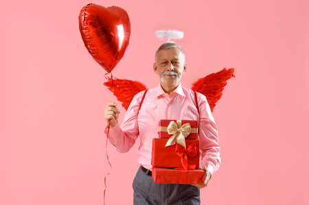 Mature man dressed as Cupid with balloon and gifts on pink background. Valentine's Day celebration