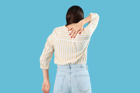 Young woman suffering from back pain on blue background