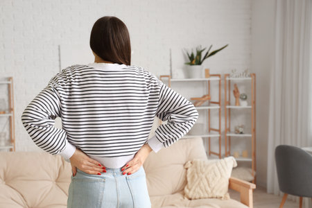 Young woman suffering from back pain at homeの写真素材