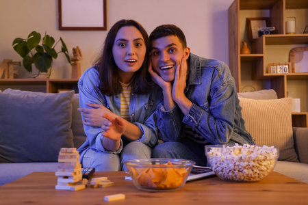 Young couple watching TV on sofa at home in eveningの写真素材