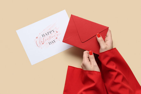 Female hands with red manicure, envelope and festive postcard on beige background. Valentine's Day...