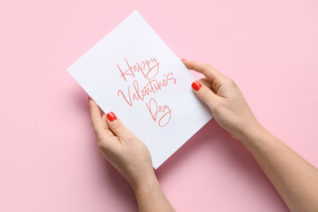 Female hands with red manicure and festive postcard on pink background. Valentine's Day celebrationの写真素材