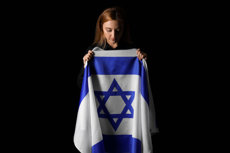 Mature woman with flag of Israel praying on black background. International Holocaust Remembrance Dayの写真素材
