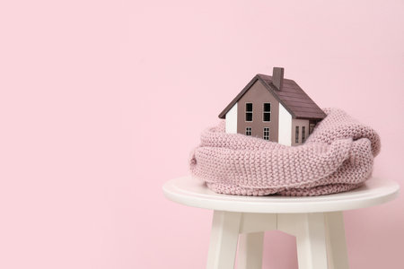 Decorative house with scarf on stool against pink background. Winter heating conceptの写真素材
