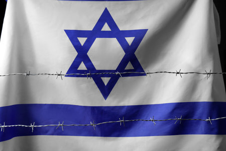 Flag of Israel behind barbed wire on black background, closeup. International Holocaust Remembrance Dayの写真素材