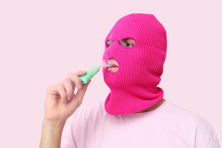 Handsome young man in balaclava with disposable electronic cigarette on pink backgroundの写真素材