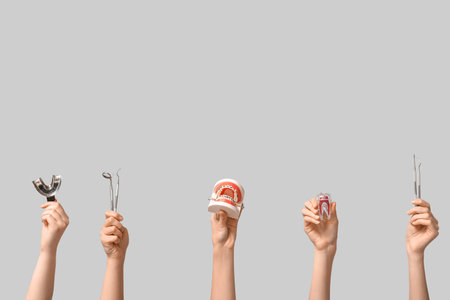 Female hands with jaw model, plastic tooth and dental tools on gray background