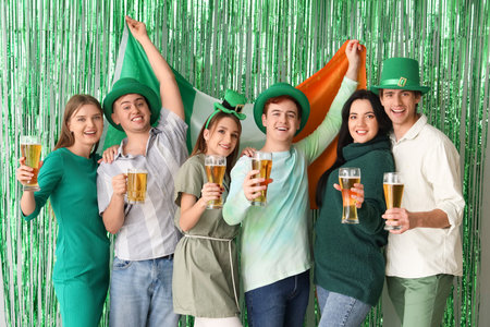 Group of young people with beer and Irish flag against green tinsel. St. Patrick's Day celebrationの写真素材