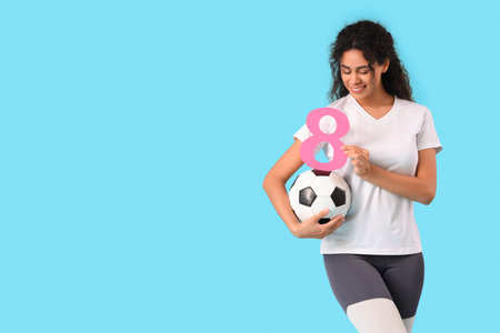Young African-American woman in sportswear with figure 8 and soccer ball on blue background....