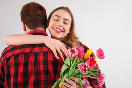 Happy young woman with tulip flowers hugging her boyfriend on white backgroundの写真素材