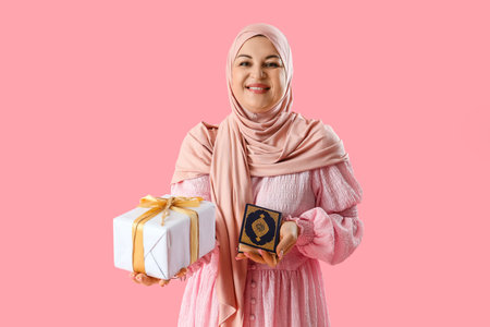 Mature Muslim woman with Koran and gift box on pink background. Ramadan celebrationの写真素材