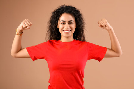Beautiful young happy African-American woman showing muscles on beige background. Women history monthの写真素材