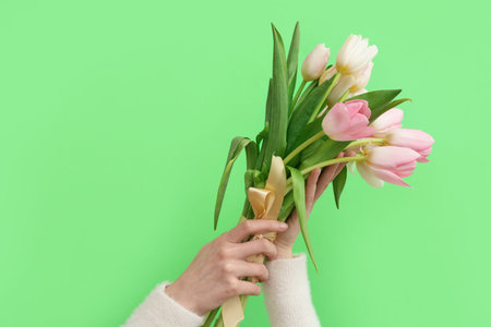 Female hands with bouquet of beautiful tulips on green background. International Women's Day