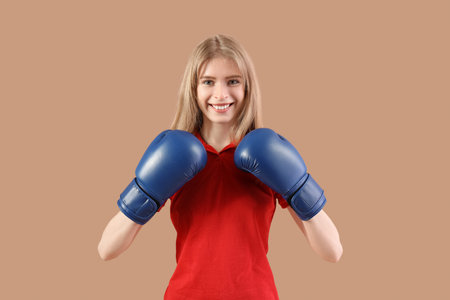 Beautiful young happy woman in boxing gloves on beige background. Women history month