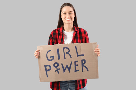 Beautiful young happy woman holding paper with text GIRL POWER on gray background. Women history monthの写真素材