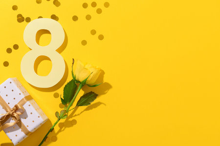 Figure 8 with gift box and beautiful rose on yellow background. International Women's Day