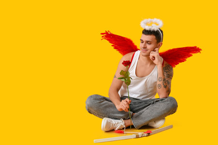 Young man dressed as Cupid with rose sitting on yellow background. Valentine's Day celebrationの写真素材