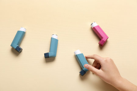 Child's hand with asthma inhalers on beige background