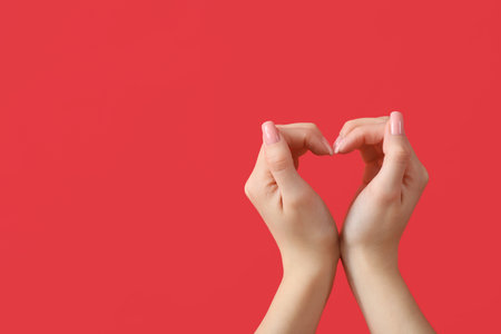 Female hands showing heart gesture on red background. Valentine's Day celebrationの写真素材