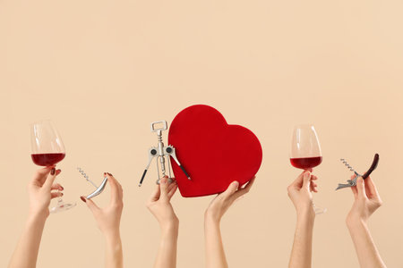 Women with glasses of wine, gift and corkscrews on beige background. Valentine's Day celebrationの写真素材