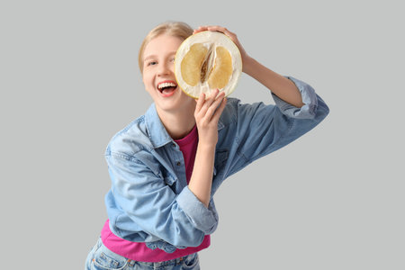 Young woman with half of pomelo on light gray background