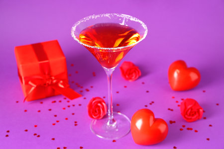 Glass of tasty cocktail with hearts, roses and gift on purple background, closeup. Valentine's Day celebrationの写真素材