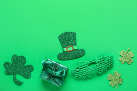 Paper clovers with leprechaun's hat, gift box and plastic eyeglasses on green background. St. Patrick's Day celebrationの写真素材