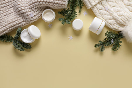 Jars of cream with Christmas decorations and warm winter clothes on pale yellow backgroundの写真素材