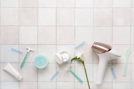 Modern photoepilator with cosmetic products, wax strips and razors on white tile backgroundの写真素材