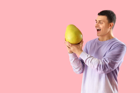 Young man with pomelo on pink backgroundの写真素材