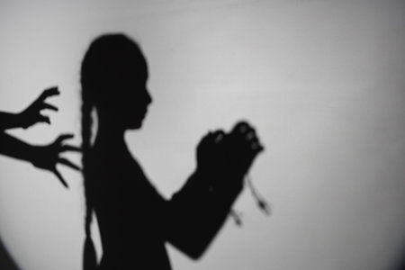 Shadow of little Jewish girl with barbed wire and hands on light background. International Holocaust...