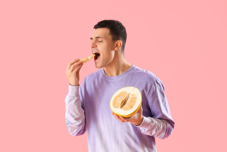 Young man eating pomelo on pink background