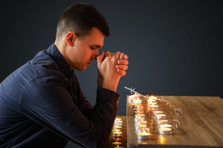 Young Jewish man with burning candles praying on black background. International Holocaust...
