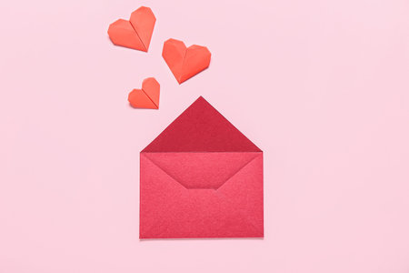 Composition with envelope and red paper hearts on pink background. Valentine's Day celebration