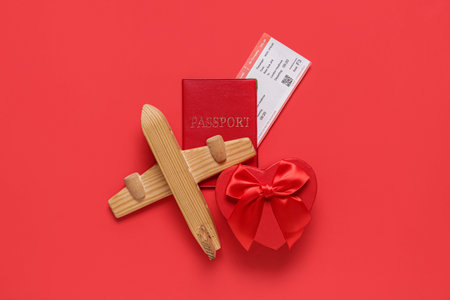 Gift box with passport, ticket and wooden airplane on red background. Valentine's Day celebrationの写真素材